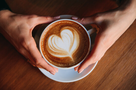 Overhead view of a Woman sitting at a table holding a latte coffee with a heart shaped decoration