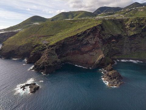 Aerial view of the rugged Playa de Nogales coastline where emerald green slopes meet the deep blue Atlantic ocean, La Palma, Canary Islands, Spain.
