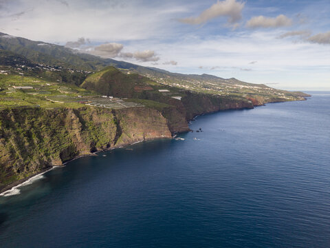 Aerial view of dramatic Playa de Nogales cliffs plunging into the deep blue Atlantic, where verdant hills meet the rugged coastline, La Palma, Canary Islands, Spain.
