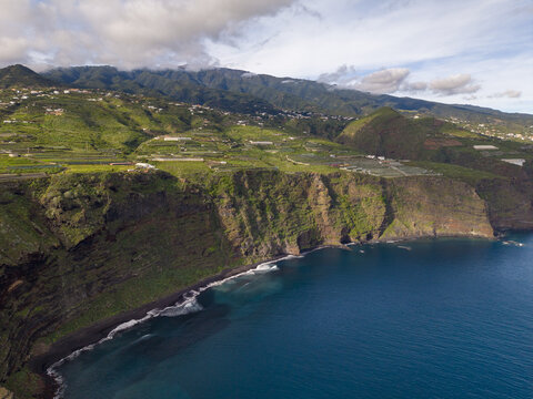 Aerial view of dramatic Playa de Nogales cliffs plunging into the deep blue Atlantic, where verdant hills meet the rugged coastline, La Palma, Canary Islands, Spain.