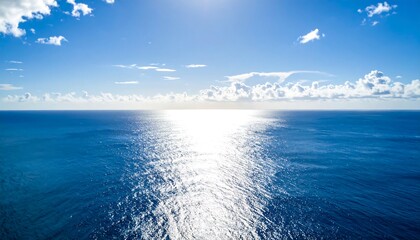Obraz premium Aerial view of a vast, tranquil ocean under a bright, cloud-dotted sky with the sun reflecting brilliantly on the water's surface