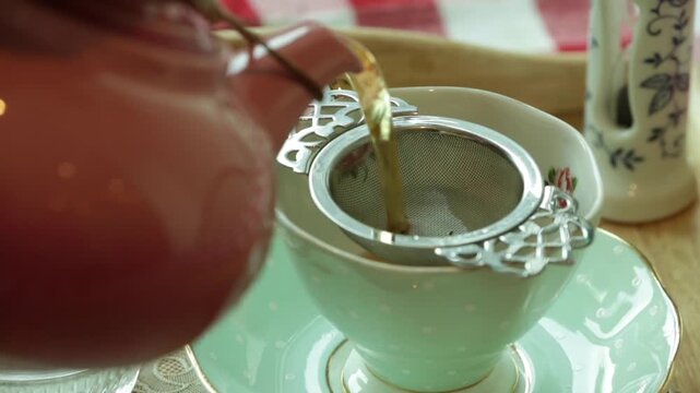 Pouring hot tea through a silver strainer into a vintage porcelain cup