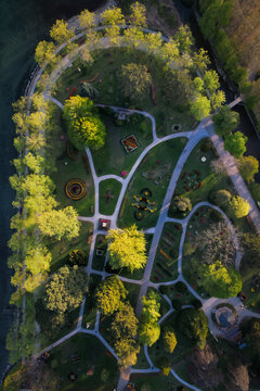 Aerial view of winding pathways carving through vibrant green spaces and mature trees, creating a tapestry of light and shadow in Parc de l'Independance, Morges, Vaud, Switzerland.