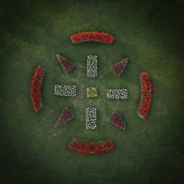 Aerial view of vibrant red and white flowerbeds arranged in geometric patterns against the deep green grass, Parc de l'Independance, Morges, Vaud, Switzerland.