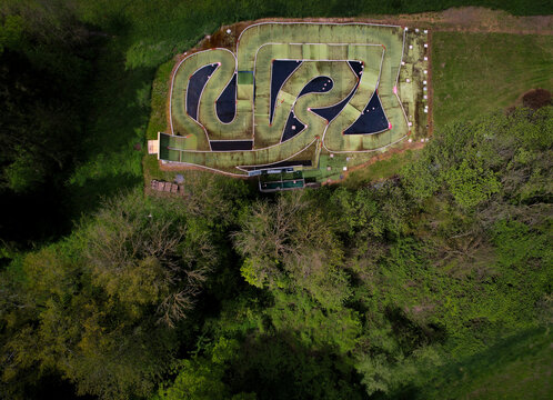 Aerial view of a miniature racing circuit, with its winding track and dark pools, contrasting with the surrounding lush green foliage, Eclepens, Vaud, Switzerland.