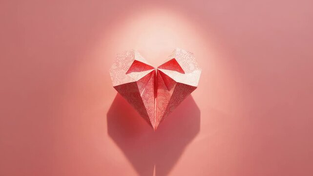 Shifting spotlight illuminating origami paper heart on pink studio wall, revealing changing shadow