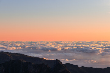 Sunrise above sea of clouds and mountain ridge in Sao Roque do Faial Madeira Portugal, gentle dawn light reveals layered peaks floating over soft cloud ocean
