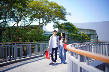 Fototapeta premium Beautiful couple enjoy shopping together, young couple holding shopping bags, Shopping, Couple, Love, Man and woman with shopping bags are hugging and smiling while walking down the Rooftop walkway