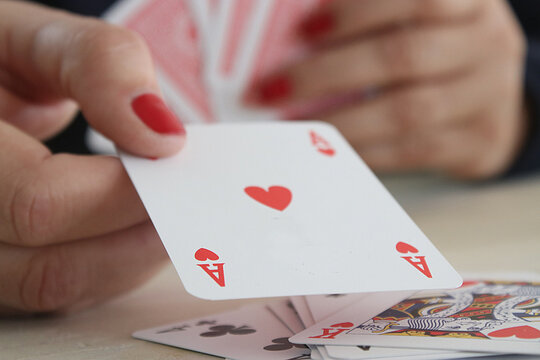 Close-up of a Woman's hand holding an ace of hearts playing card in a card game