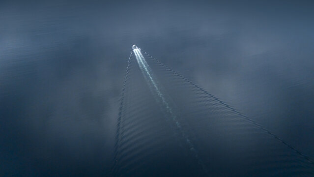 Aerial view of a lone boat slicing through the inky waters, leaving a shimmering trail in its wake, Torshamn, Faroe Islands.