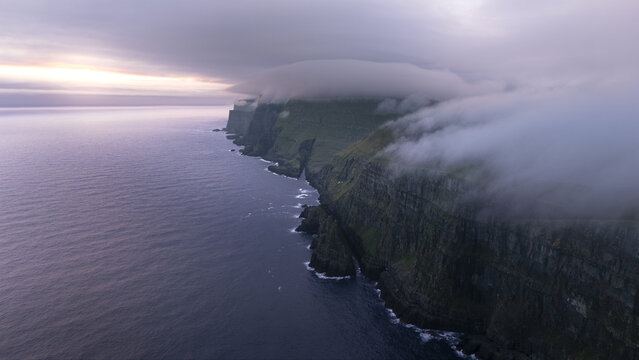 Aerial view of dramatic cliffs meeting the moody ocean under a blanket of fog, Torshavn, Faroe Islands.