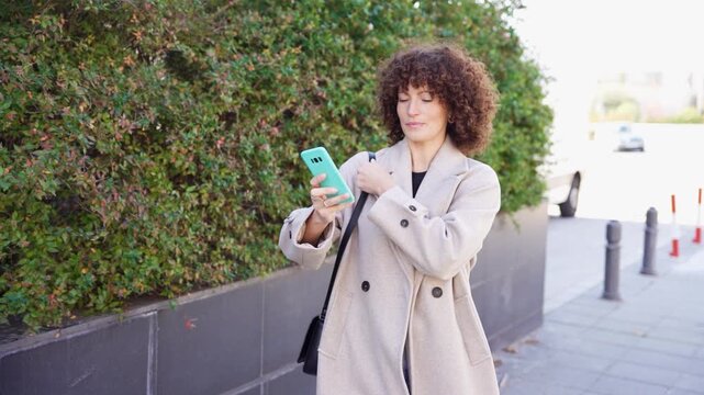 A Stylish Woman Dressed in a Casual Outfit Poses Beautifully Against Urban Greenery