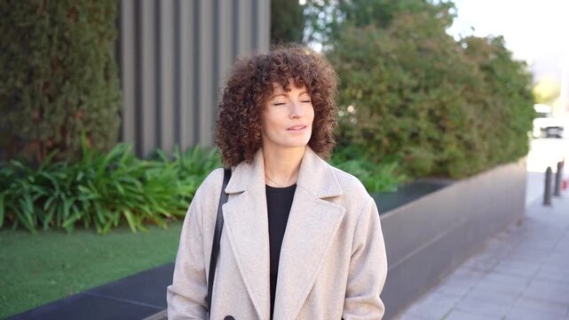 A Fashionable Woman Sporting Curly Hair in an Urban Setting Surrounded by Greenery
