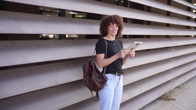 A young woman uses her tablet against a modern backdrop, reflecting her casual techsavvy lifestyle