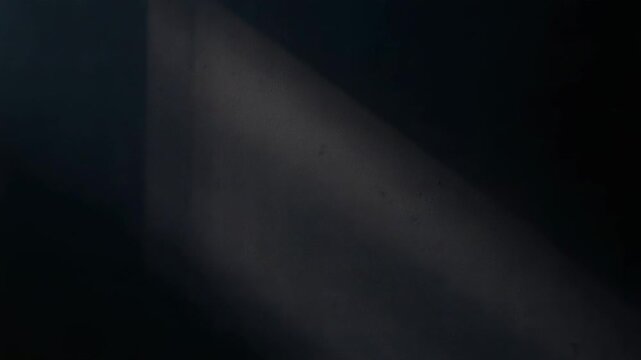 Narrow window slit sending diagonal shaft of pale light into dark room, highlighting dust haze