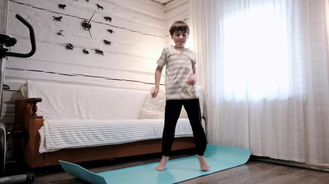 A schoolboy practices a Cris cross movement from a breakdancing lesson at home. Dancing hobby. A boy jumps up and crosses his legs. Athletic 9 year old child. Sports warm-up. High quality 4K footage.