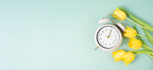 Switch to daylight saving time in spring, summer time changeover, alarm clock with yellow tulip flowers