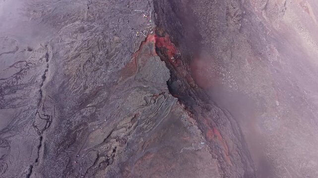 Drone footage aerial view over fractured lava formations at Dolomieu Crater, part of Piton de la Fournaise on Reunion Island. The shot highlights volcanic fissures, oxidized rock textures and mist.