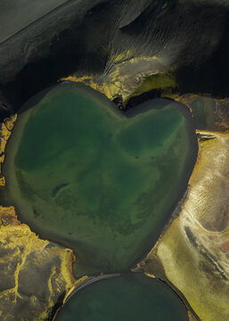 Aerial view of an emerald heart-shaped lake nestled amidst the stark, textured earth, a serene jewel in a rugged landscape, Selfoss, Iceland.