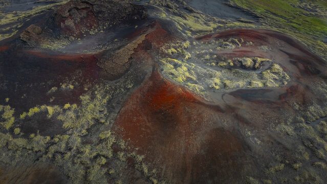 Aerial view of a volcanic landscape reveals a tapestry of fiery red earth and patches of mossy green, creating a starkly beautiful contrast, Iceland.