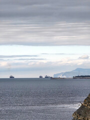Cargo ships on horizon near rocky coastline