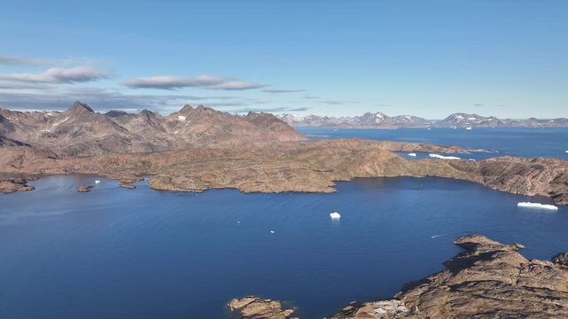 Aerial footage of Tasiilaq, a remote coastal city in eastern Greenland, showcasing colorful houses along the shoreline, dramatic mountain landscapes, and the calm Arctic Ocean. Captured from above
