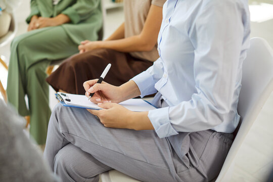 Women group meeting in business training circle. Close-up of participant employee taking notes on clipboard as others share ideas. Focus on learning and communication in office. Teamwork concept.