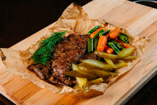 Close-up of Beef en papillote with gherkins, beans and carrots on a wooden chopping board