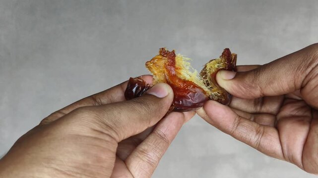 Hand holding organic and fresh dried brown dates fruit isolated on white background split it to check the quality. Weight loss and healthy diet sweet snack concept. Extreme closeup side view.