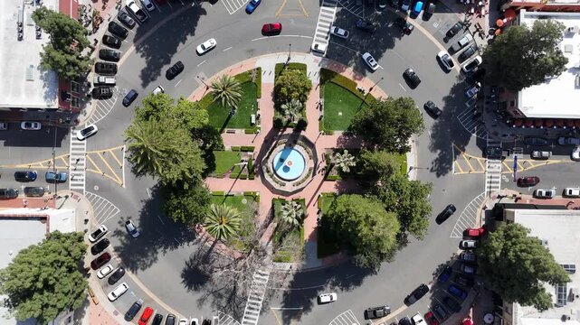 Aerial view of a roundabout with a water fountain surrounded by green trees and buildings under the bright sun, Orange, California, United States.