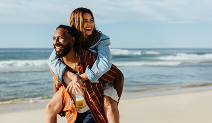 Couple enjoying a piggyback ride together on a sunny day at the beach