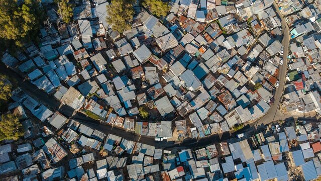 Aerial view of informal settlement's corrugated iron roofs glinting under the sun, a stark contrast to the green hills in the background, Cape Town, Western Cape, South Africa.