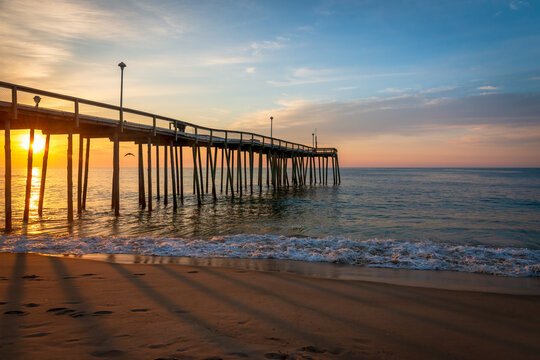 Ocean City, Maryland, USA - 26 June 2014 - Photo showing a wooden pier at sunset with light waves and a sandy beach in Ocean City, Maryland.