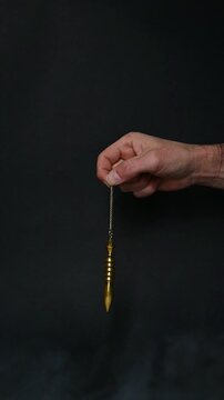 Golden Egyptian Isis Pendulum Moving Through Smoke on Black Background, Radiesthesia, Intuition and Subtle Energy Concept