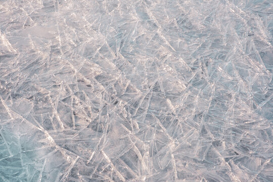 Abstract background of the surface of frozen water with natural cracks and ice crystals. Close-up, full frame. Perfect for winter themes, cool concepts and minimalist design.