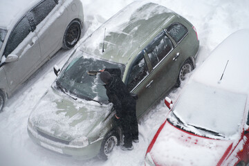 Winter car maintenance. A man is brushing snow off a vehicle.