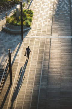 View of a lone figure walking along a geometrically patterned walkway, bathed in the warm glow of the late afternoon sun, Punggol, Singapore.