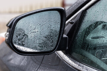 A detailed close-up of a wet car side mirror and window