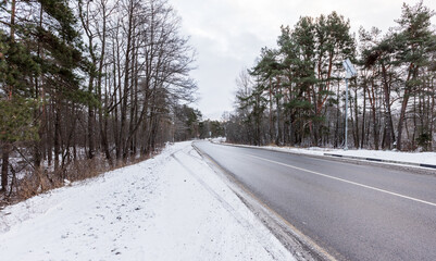 Obraz premium A quiet winter scene features a snow-dusted road winding through a forest