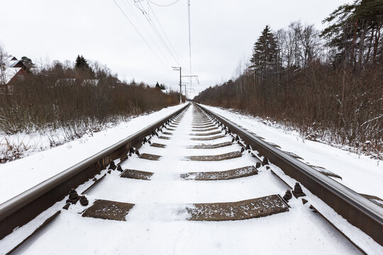 Snow-covered railway tracks extend toward the horizon, flanked by bare trees