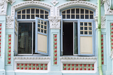 decorative facade detail from a heritage building in Singapore. Two open windows are framed by pastel blue and cream molding, with arched transoms 