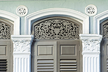 refined architectural detail from a heritage building on Geylang Road, Singapore. The facade features three arched openings framed by ornate plasterwork, with floral and geometric carvings 