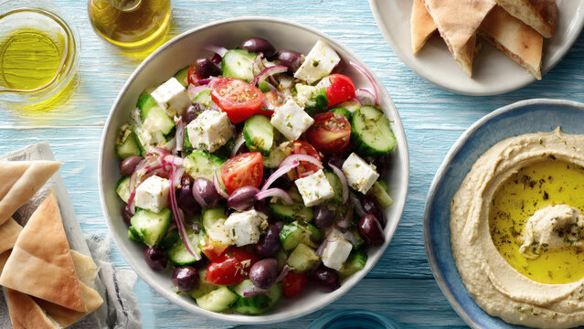 A refreshing flat lay of a large Greek salad with olives, feta, and pita on a blue wooden surface viewed from directly above