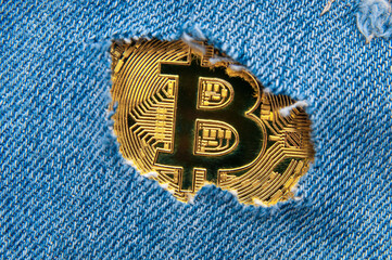 Golden bitcoin coin in torn denim patch close up