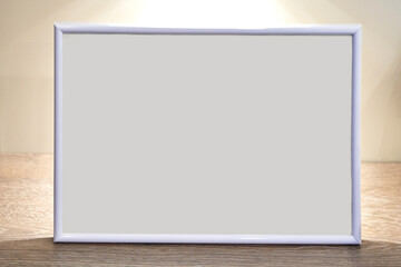 Fototapeta premium Blank white photo frame on wooden surface with soft lighting in simple neutral setting.