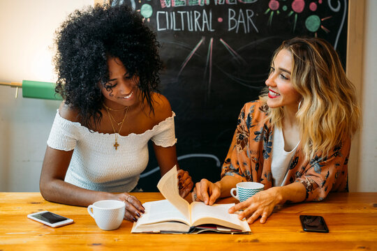 Diverse women friends reading book conversing at cultural bar