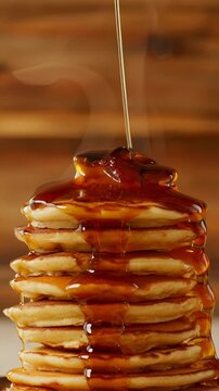 A tall stack of golden pancakes receives a generous pour of glistening syrup