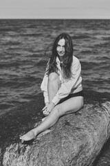 Young woman portrait sitting on rock by Baltic Sea in natural light