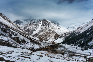 Obraz premium Scenic snowy valley with mountain pass, curving road, and winter landscape surrounded by steep slope
