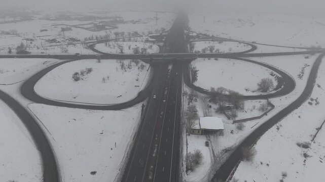 4K 60fps aerial view of a highway cloverleaf interchange in winter fog, cinematic snow-covered road infrastructure.